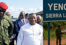 Yenga Border Reopens as Sierra Leone, Guinea Renew Bilateral Cooperation A delegation of officials walking outdoors, led by a man in a white suit, with soldiers nearby, at a Yenga border site in Sierra Leone.