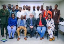 SLCAA Strengthens Aviation Safety with ICAO Dangerous Goods Training for 14 Inspectors A group of about 16 diverse professionals pose for a group photo in a conference room, seated in the front row and standing behind, with a projector screen and a logo in the room background.