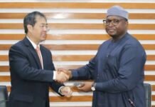 China Donates 15 Protocol Vehicles to Support Sierra Leone’s ECOWAS Summit Two men in formal attire shake hands across a table during a meeting; Chinese and Nigerian flags are visible on the table.