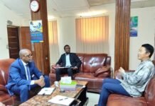 Labour Ministry, Chinese Embassy Agree on Stronger Cooperation and Work Permit Reforms Three men in a formal meeting sit on brown leather couches in a bright office, discussing at a coffee table with documents and a laptop nearby.