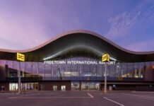 …Ahead of ECOWAS Summit SLCAA Announces Temporary Airport Security Measures, Assures Uninterrupted Commercial Flights Front view of Freetown International Airport terminal at dusk with a curved roof, glass facade, and gate signs 3C and 3R.