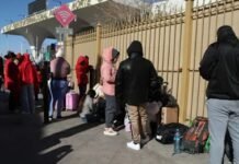 US Lists 26 Sierra Leoneans Among 374 West Africans Facing Deportation Line of people with suitcases and bags waiting outside a fenced area at a transit station on a sunny day.