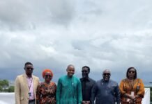 Africell, Government and UNDP Unveil UniPod to Accelerate Youth Innovation Six people stand in a row on a rooftop, wearing colorful traditional African outfits under a cloudy sky – group portrait.