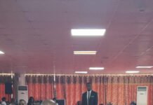NPRA DG Briefs Parliament on Downstream Petroleum Sector Developments Man in a blue suit speaks into a microphone beside a man in orange traditional attire at a conference panel, with audience seated behind them.