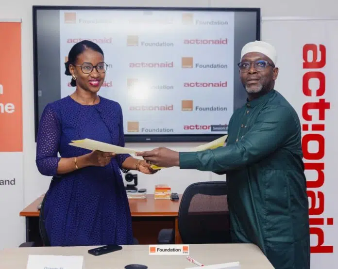 Two professionals exchange documents in an office setting with ActionAid Foundation branding in the background.