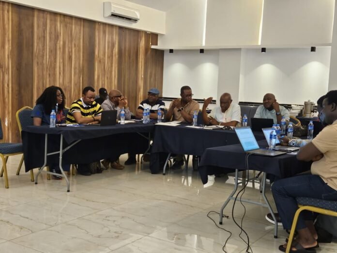 Group of diverse professionals seated around a long conference table, discussing with laptops and water bottles in a bright room.