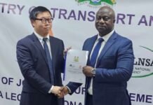 Transport Minister Secures Landmark Shipping Investment from China’s Zhejiang Xiehai Group Two men in suits shake hands while one presents a document at a formal ceremony.