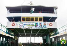 SLPHA Supports ECOWAS Mid-Year Summit with Seamless Ferry Operations and Exceptional Hospitality Two-level white ferry docked at a pier, with yellow-framed windows and a banner across the front deck and lifebuoys on both sides.