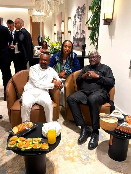 Three adults seated in brown chairs at a lounge, with snacks and orange juice on a small table nearby.