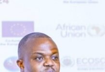 CHRDI Urges Full Implementation of African Human Rights Court Protocol Man in a blue suit and pink tie speaks into a microphone at a conference, wearing a lanyard; blurred backdrop shows EU and African Union logos.