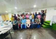 Government, ECOWAS and ILO Strengthen Protection for Domestic Workers in Sierra Leone Group of diverse adults posing for a group photo in an indoor meeting hall with tables and chairs nearby.