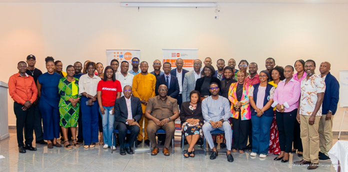 Large diverse group of adults posing for a group photo in a conference room, with banners in the back indicating a formal event.