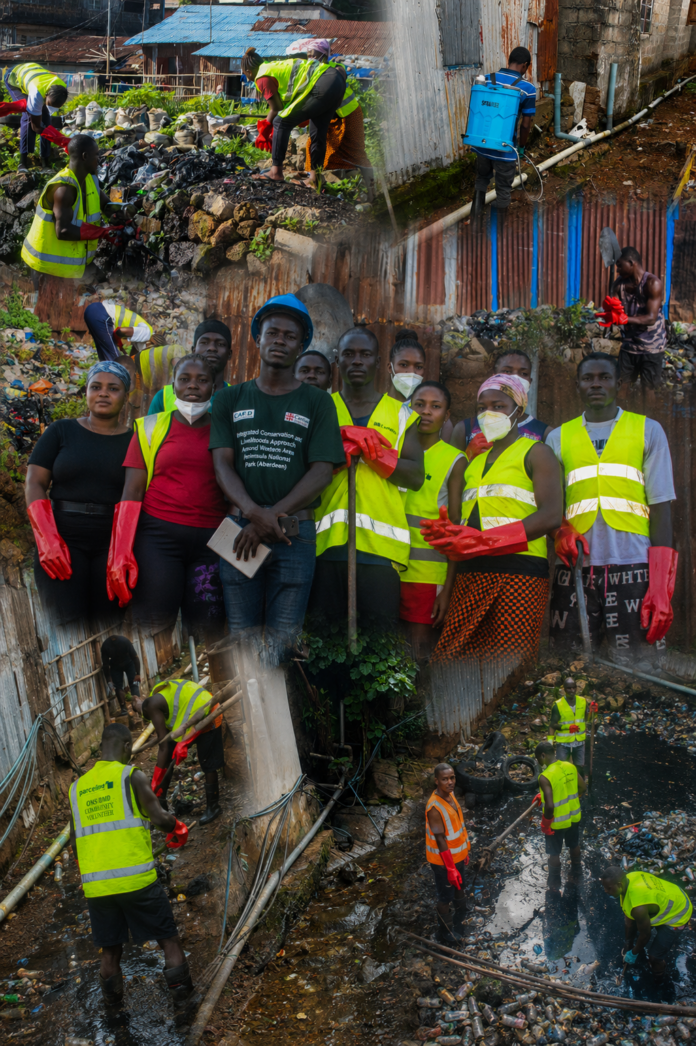 Group of volunteers in bright safety vests and red gloves cleaning a trash-filled canal, with more workers in the background.