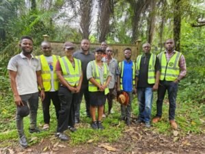 Group of people wearing high-visibility vests posing outdoors in a lush, wooded area.