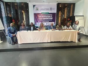 | The Calabash Newspaper Eight people seated at a long conference table in front of a banner that reads 'The Ratification of 6 ILO Conventions' and related logos.