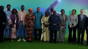 | The Calabash Newspaper Diverse group of professionals posing for a photo at a conference event against a colorful backdrop on a green carpet.
