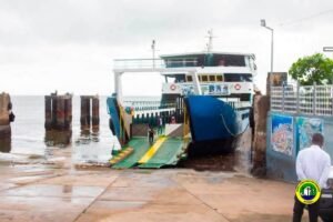 | The Calabash Newspaper Blue and white passenger ferry docked at a jetty with a green and yellow boarding ramp lowered to the water's edge.