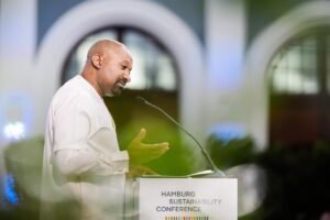 Vice President, Dr. Mohamed Juldeh Jalloh | The Calabash Newspaper Man in a white shirt speaks at a podium labeled Hamburg Sustainability Conference, microphone extended toward him.
