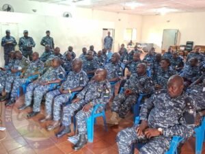 Group of uniformed personnel in blue digital camouflage seated in a conference room, likely at a briefing or meeting.
