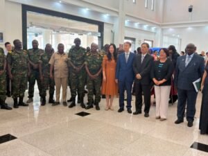 | The Calabash Newspaper Group of soldiers in camouflage uniforms and civilian officials in suits and dresses posing for a formal photo in a bright indoor lobby.