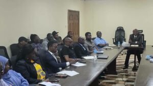 | The Calabash Newspaper A group of professionals seated around a long conference table while a man at the head leads a meeting.