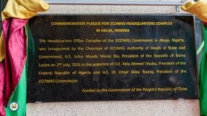 Commemorative plaque for ECOWAS Headquarters Complex in Abuja, Nigeria; describes inauguration and China funding; framed by colorful cloths.