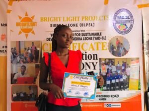 Young woman in a red blouse poses with a certificate of completion at a Bright Light Projects event backdrop.