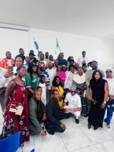 | The Calabash Newspaper Large group of men and women posing for a group photo indoors, some in traditional attire, with Nigerian flags in the background.