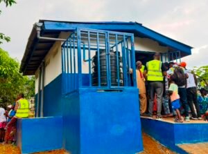 People queueing around a blue elevated water tank and building, some wearing safety vests, in a rural distribution site