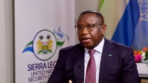 President Bio takes an interview with China Media Group in New York | The Calabash Newspaper Man in a dark pinstripe suit and red patterned tie speaks in an interview, with a Sierra Leone banner in the background.