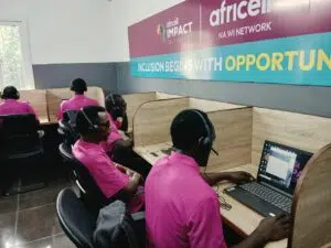Call center staff in pink shirts wearing headsets at individual computer desks under a banner that reads 'Inclusion Begins with Opportunity.'