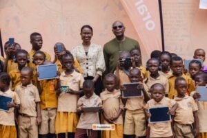 | The Calabash Newspaper Group of schoolchildren in beige uniforms holding tablets for a photo, with two adults and a Foundation banner in the background.