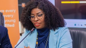 Woman with curly hair and glasses in a blue blazer speaks into a microphone at a panel discussion.