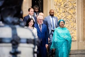 | The Calabash Newspaper Group of formally dressed people descending a stone staircase in a grand, ornate building; woman in turquoise leads the way.