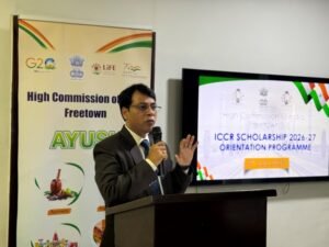 | The Calabash Newspaper Man in a suit speaks at a podium during a presentation, with a banner and a screen showing ICCR Scholarship Orientation Programme.