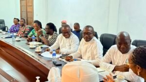 | The Calabash Newspaper Diverse group of professionals seated along a long conference table in a meeting room, with notebooks, cups, and bottles of water in front of them.