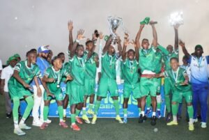 Green-clad soccer team celebrates victory, jumping with a trophy raised high and medals around their necks on a soccer field.