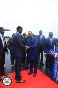 | The Calabash Newspaper Officials in formal attire shake hands on a red carpet outdoors, with a circular emblem visible in the bottom left.