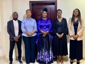 | The Calabash Newspaper Five professionals stand side by side in a hallway, dressed in business/formal attire for a group photo in front of a door.