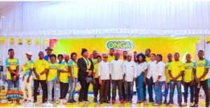 | The Calabash Newspaper Group of people posing for a photo at an ONGA event, many wearing yellow and blue shirts, with an ONGA banner behind them on a bright backdrop.