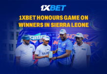 1xBet Wrapped Up Game On Promo in Sierra Leone: Winners Received iPhone 16 and Big Cash Prizes! Four men in 1XBET shirts on a stage, receiving an award, with a blue backdrop and the headline '1XBET Honours Game on Winners in Sierra Leone'