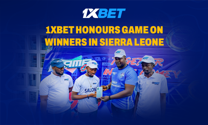 Four men in 1XBET shirts on a stage, receiving an award, with a blue backdrop and the headline '1XBET Honours Game on Winners in Sierra Leone'