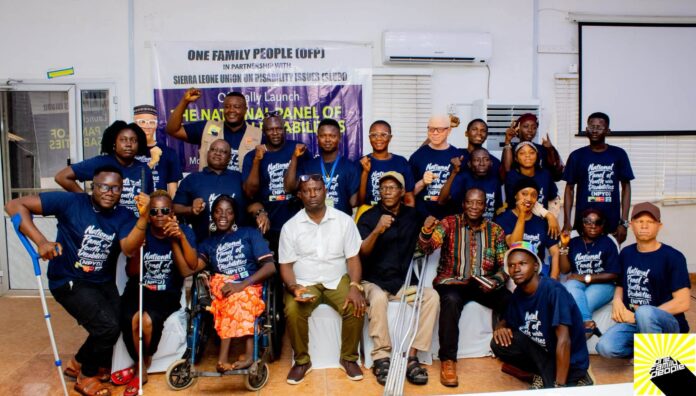 Group of diverse people posing for a banner at a disability rights event, many with fists raised in celebration.