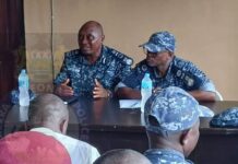 Deputy Inspector General Urges Sierra Leone Police to Uphold Professionalism and Integrity Two police officers in blue camouflage uniforms sit at a table giving a briefing; one speaks with hand gestures while others listen.