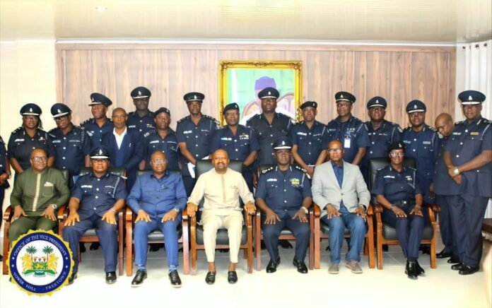 Formal group photo of police officers and officials, seated in front row with others standing behind in a conference room; portrait on the wall behind them.