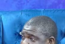 2028 or 2030? SLPP Mambu’s Reckless Remark Fuels “More Time” Suspicions Man wearing a black and white striped polo shirt sits on a blue tufted couch, talking, with a microphone clipped to his shirt.