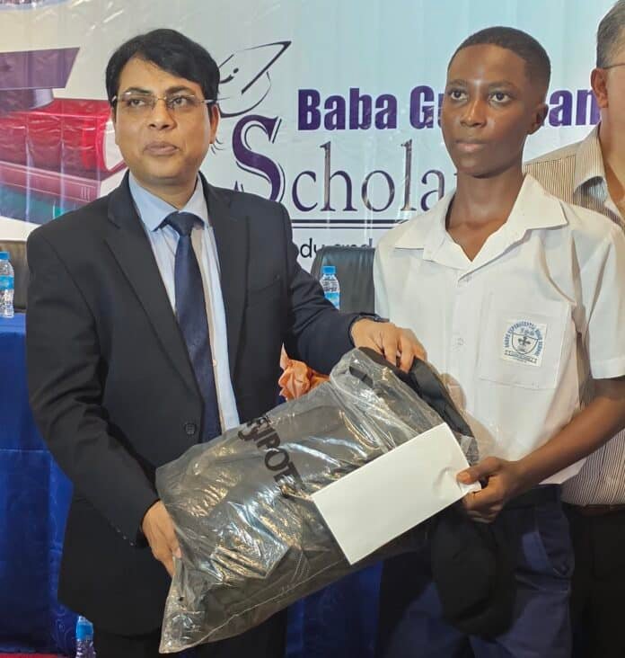 Man in a suit hands a prize to a student in a white uniform on stage, with a banner in the background.