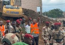 Conakry Landfill Landslide: 17 Sierra Leoneans Confirmed Dead, 54 Survivors Identified Group of soldiers in desert camouflage and red berets standing at a construction site, with a bulldozer on a dirt hill and a person in an orange safety vest gesturing to the crowd.