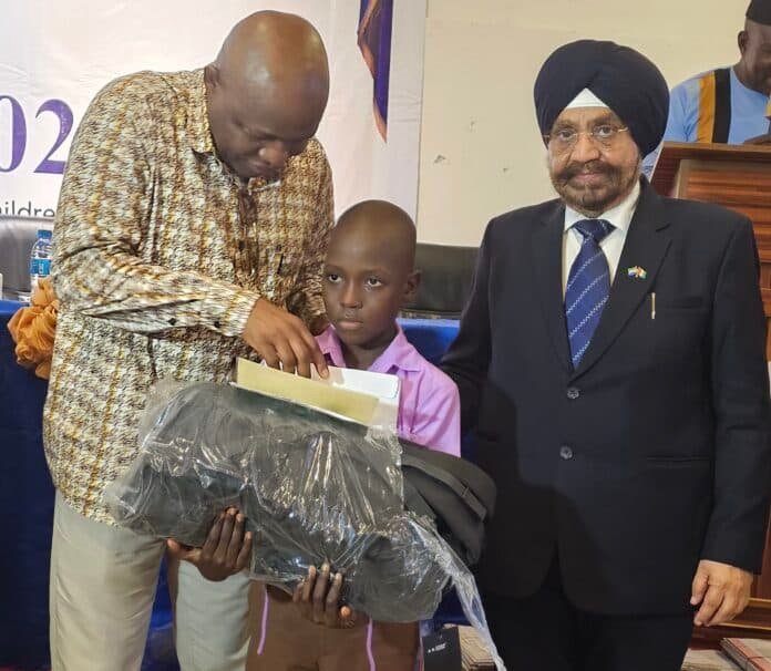 A man in a patterned shirt helps a young boy hold a large, wrapped package during a formal event, with another man in a suit nearby.