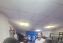 UNDP Lesotho Concludes Four-Day Peer-Learning Exchange on Sierra Leone’s Development Financing Model Group of five people standing in a bright store hallway, chatting and listening to a man in a beige outfit who is speaking.